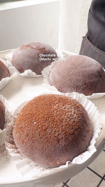 four chocolate donuts sitting on top of a white tray next to a brown bag