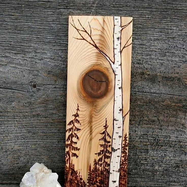 a piece of wood with trees painted on it next to some rocks and a rock