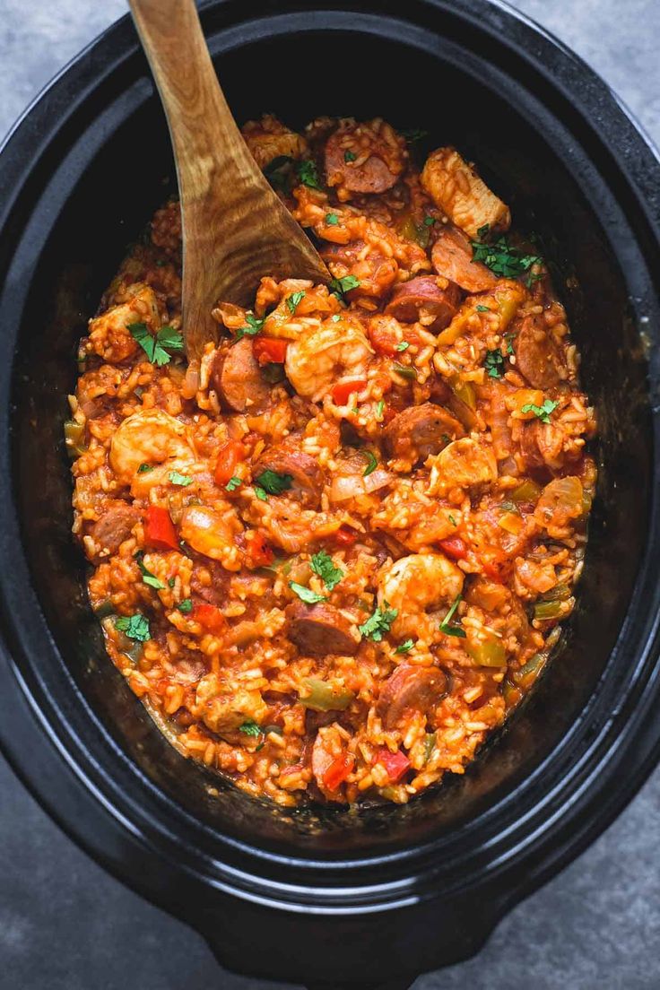 a wooden spoon in a slow cooker filled with rice and sausages, garnished with parsley