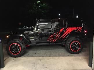 a black and red jeep parked in front of a building at night with its lights on