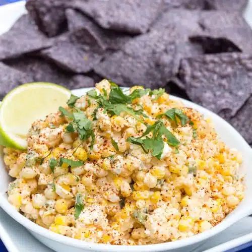 a white bowl filled with corn next to tortilla chips and lime wedges