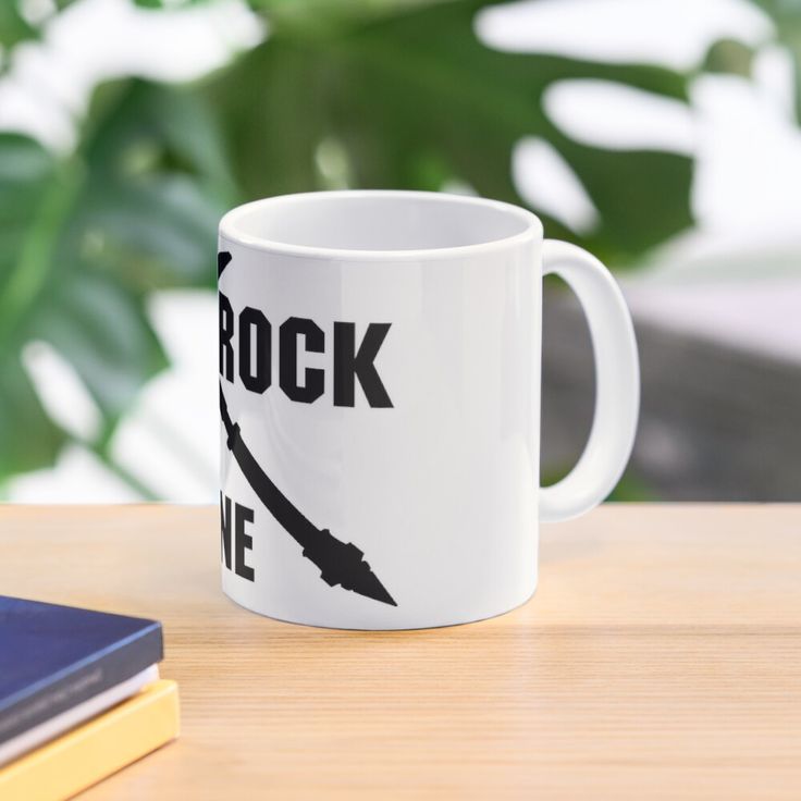 a white coffee mug sitting on top of a wooden table next to a book and plant