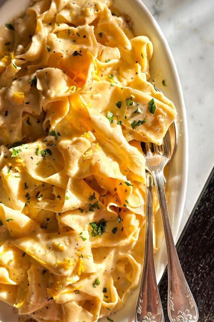 a white plate topped with pasta covered in cheese and parsley next to two silver spoons