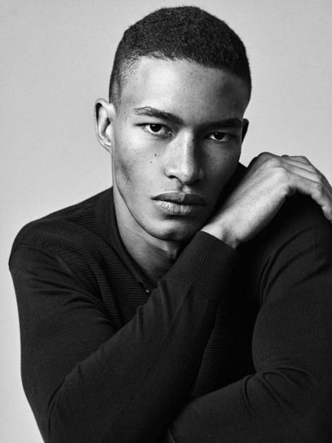 a black and white photo of a young man with his hand on his chin looking at the camera