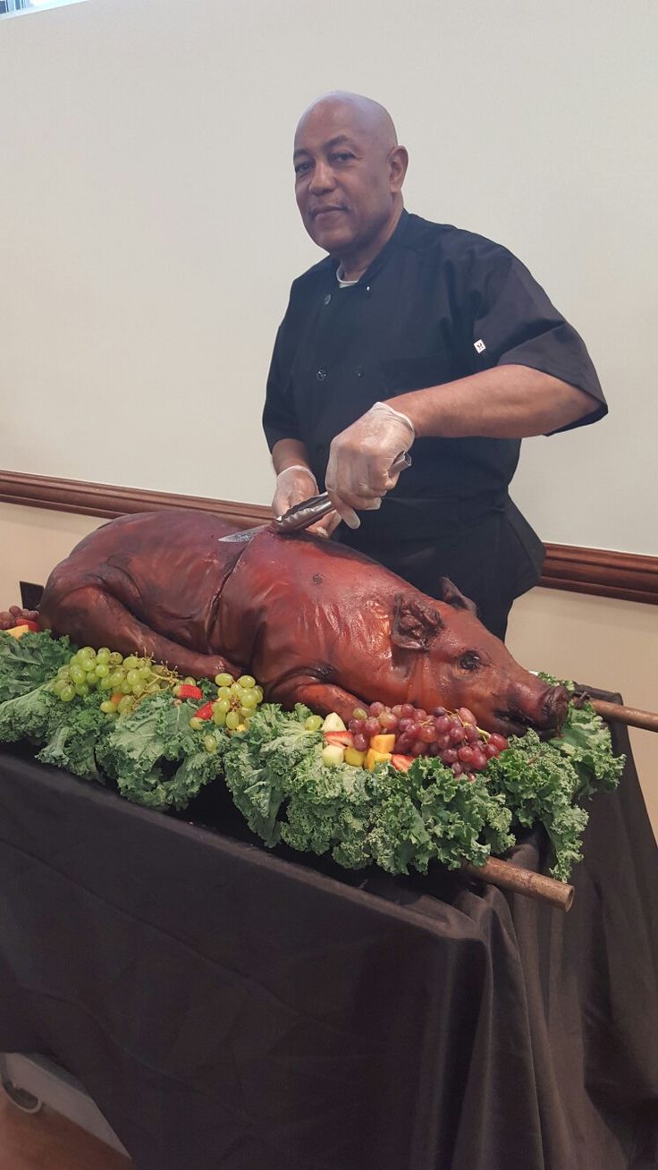 a man cutting up a large piece of meat on top of a table with vegetables