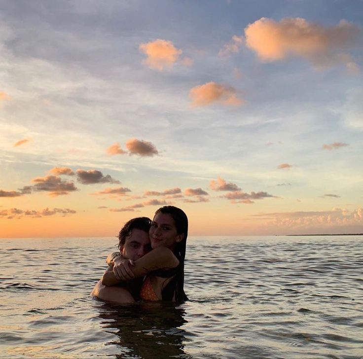 two women are hugging in the water at sunset or dawn, with clouds above them