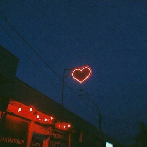 a heart shaped neon sign hanging from the side of a building in front of a dark sky