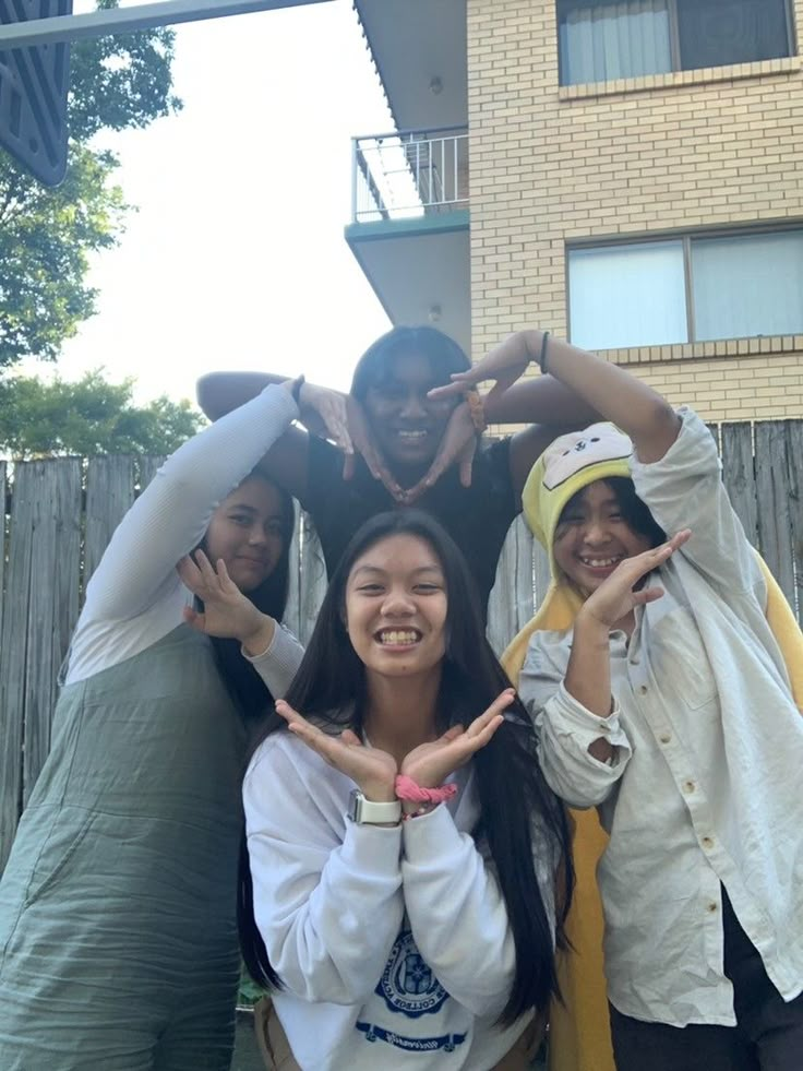 four people standing in front of a building making the v sign with their hands and smiling