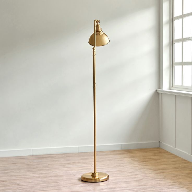 a floor lamp in an empty room with white walls and wooden floors, near a window