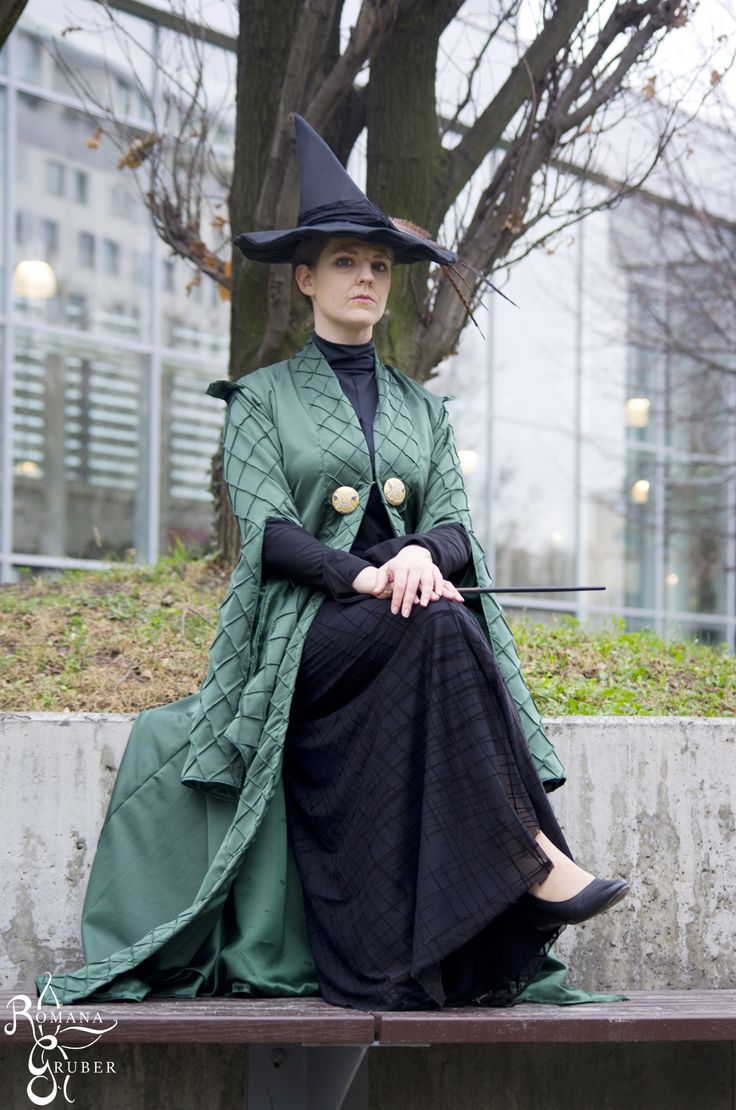 a woman sitting on top of a wooden bench wearing a green dress and black hat