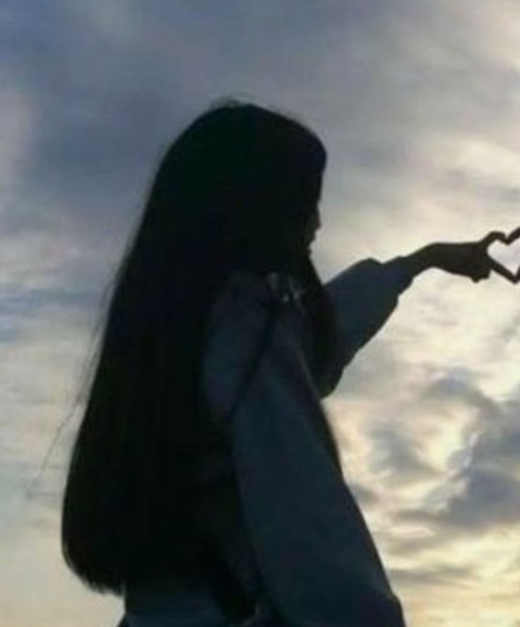 a woman with long black hair is holding her hand out in front of the sky