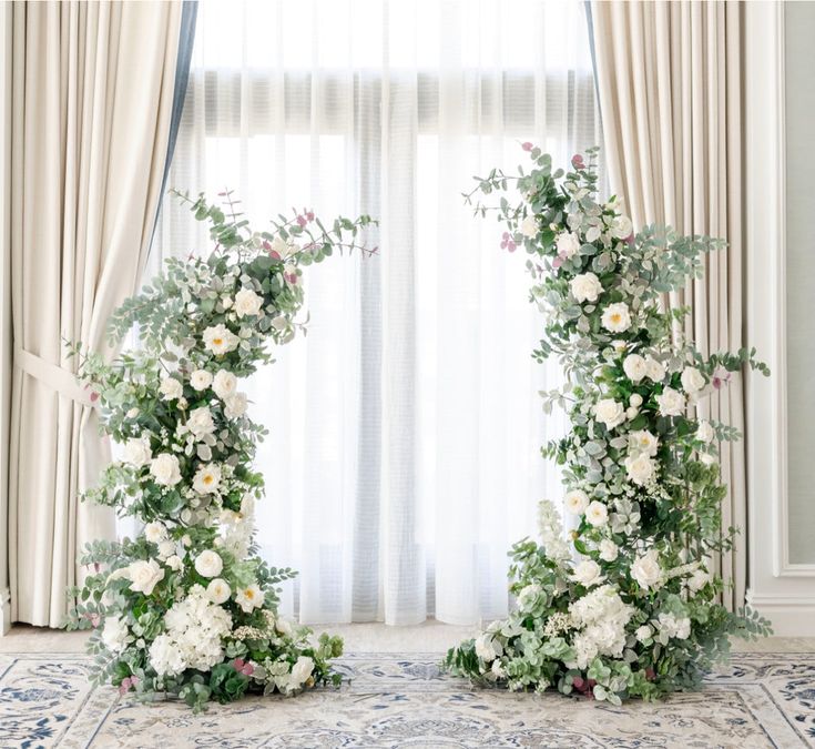 two floral archways with white flowers and greenery on the floor in front of a window