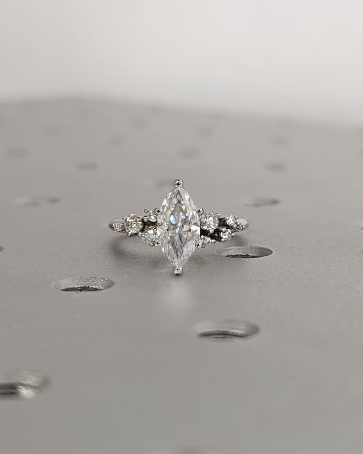 a diamond ring sitting on top of a silver surface with drops of water around it