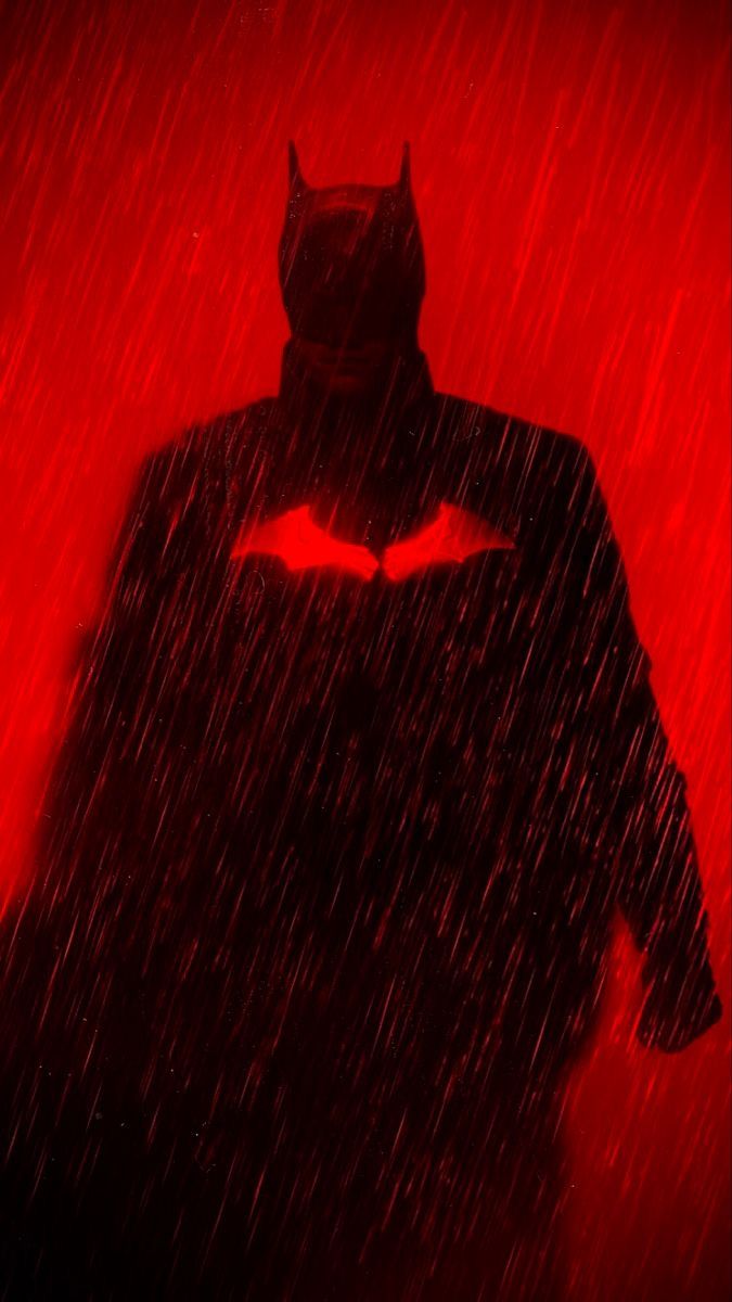 the dark knight batman silhouetted against a red background with rain falling down on it