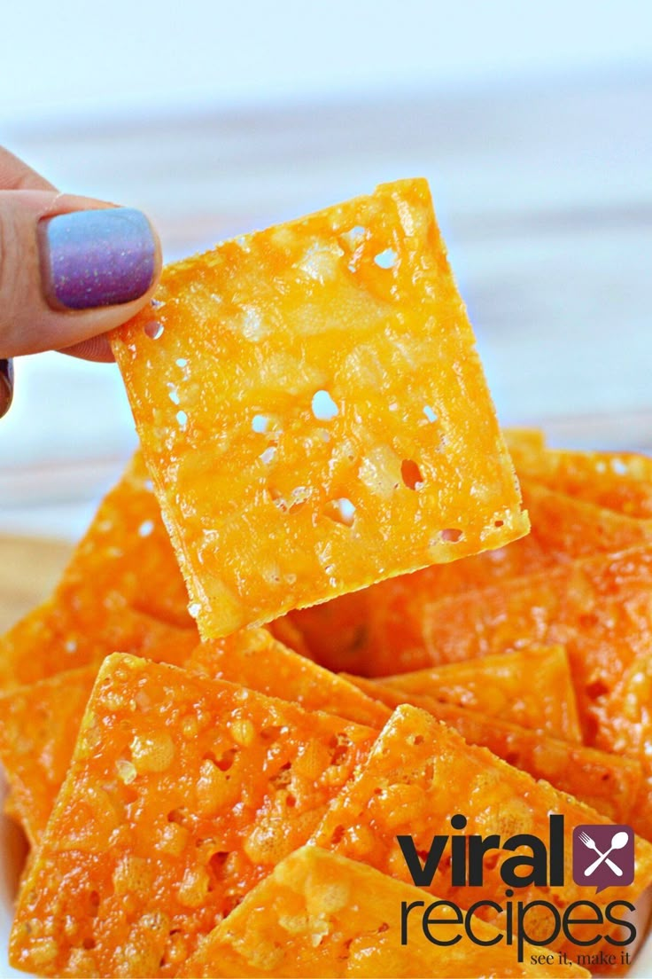 a hand holding up a square cracker over a bowl full of cheetos