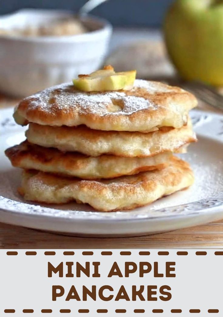 a stack of pancakes sitting on top of a white plate with apples in the background