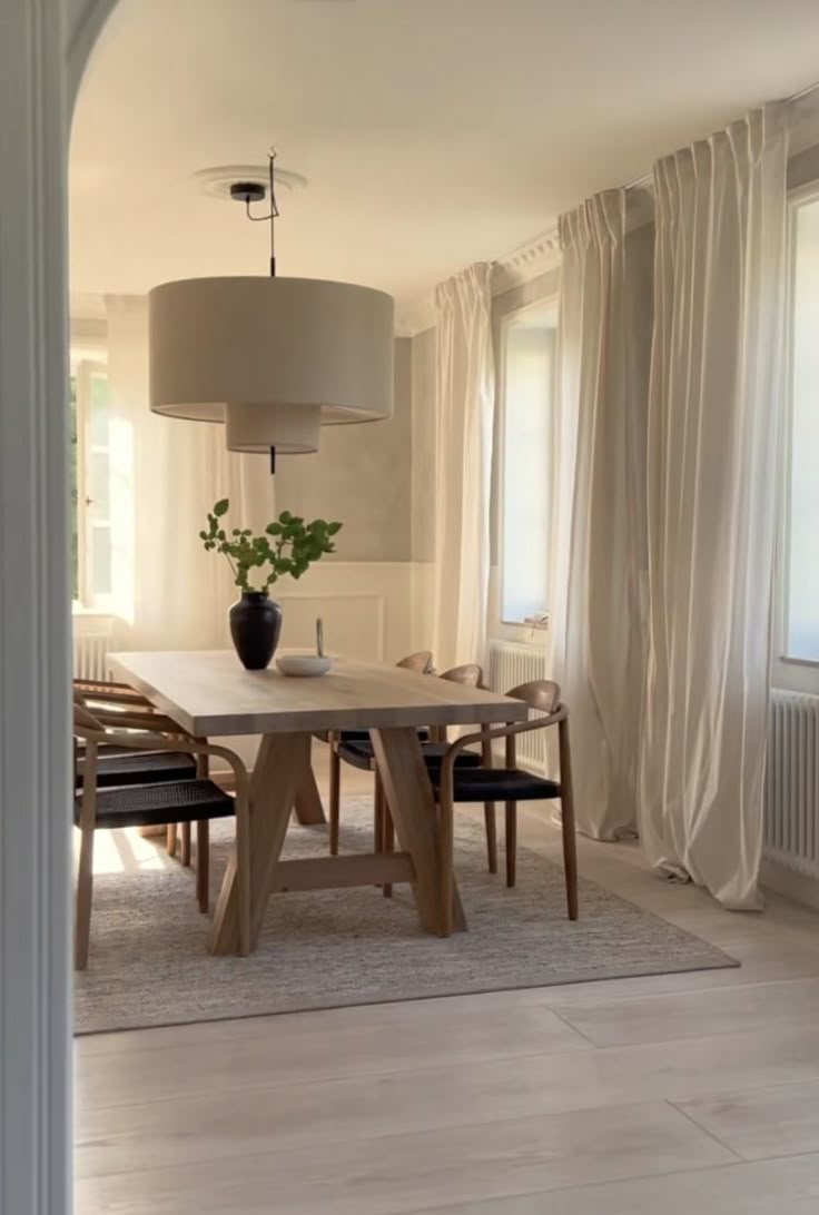 a dining room table with chairs and a vase on it in front of a window