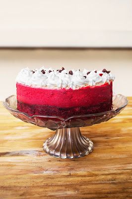 a red velvet cake with white frosting on a glass plate sitting on a wooden table