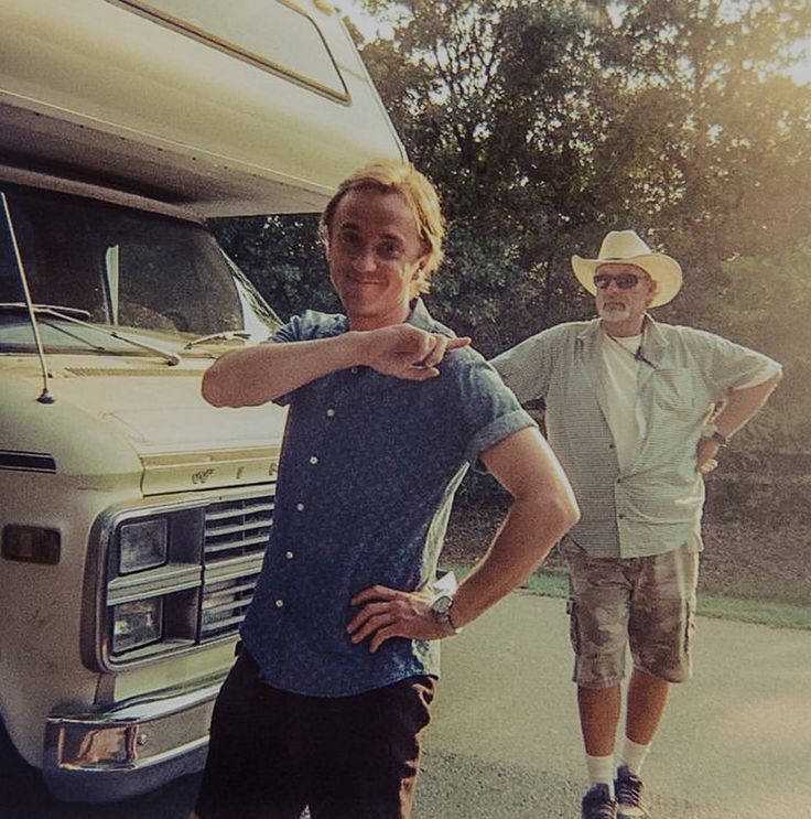 two men are standing in front of a motor home and one is pointing at the camera