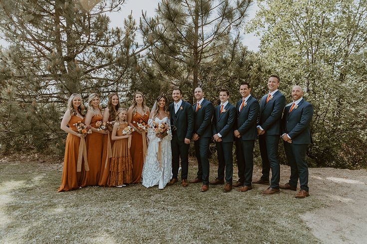 a group of people standing next to each other in front of some pine trees and bushes