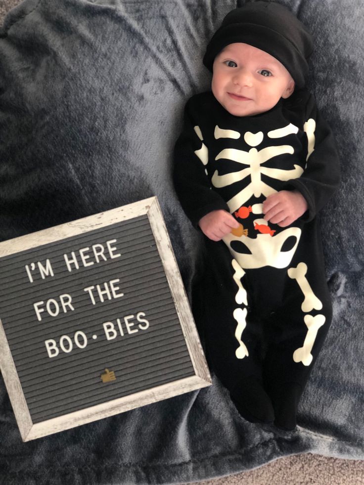 a baby in a skeleton costume next to a sign that says i'm here for the boo - bies