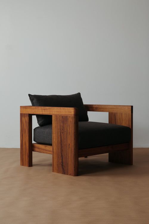 a wooden chair sitting on top of a floor next to a white wall and black pillow