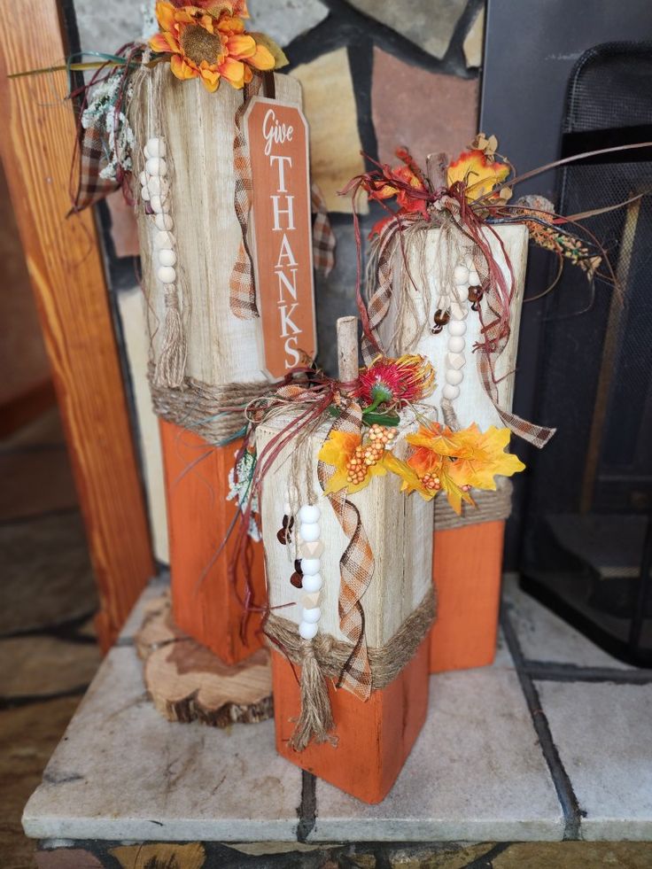 two wooden pumpkins decorated with fall flowers and burlocks are sitting in front of a fireplace