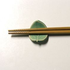 two chopsticks resting on top of a green plate next to another chopstick