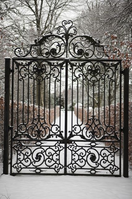 an iron gate with snow on the ground and trees in the backgrounge