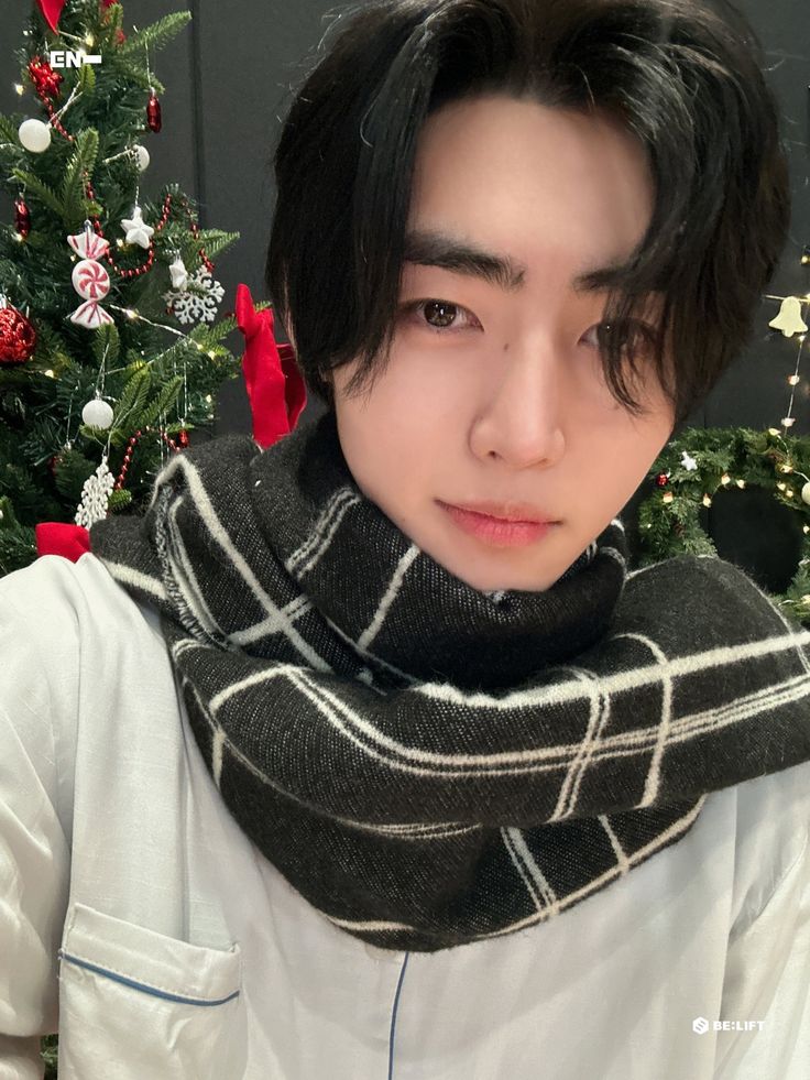 a young man wearing a scarf around his neck in front of a decorated christmas tree