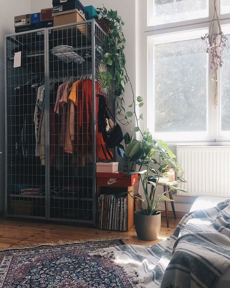 a room with a bed, rug and clothes rack in it's corner next to a window