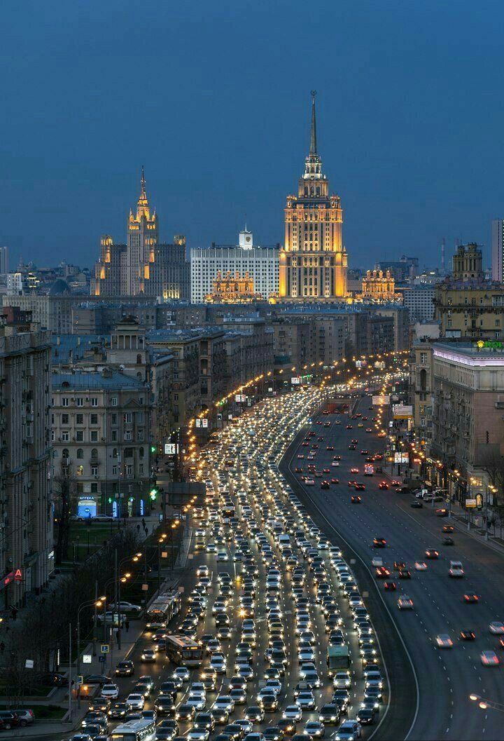 a city street filled with lots of traffic next to tall buildings at night, in the distance is a large clock tower