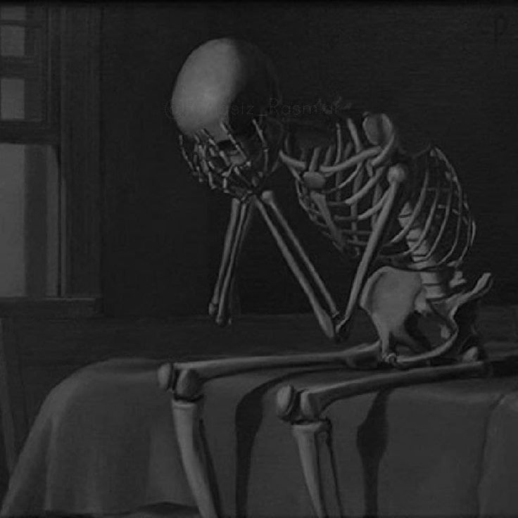 a skeleton sitting on top of a table in front of a window, with its head down