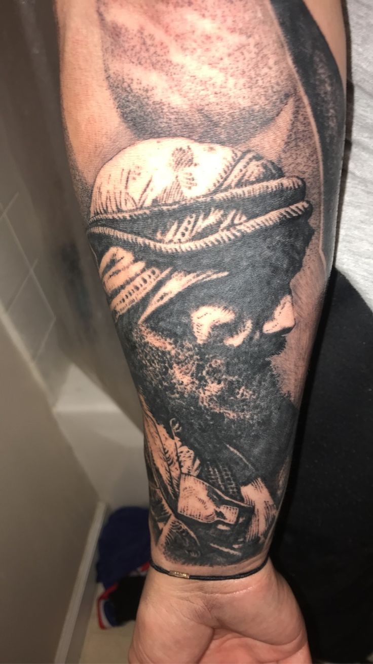 a man's arm with a tattoo on it that has a black and white image of a person wearing a hat