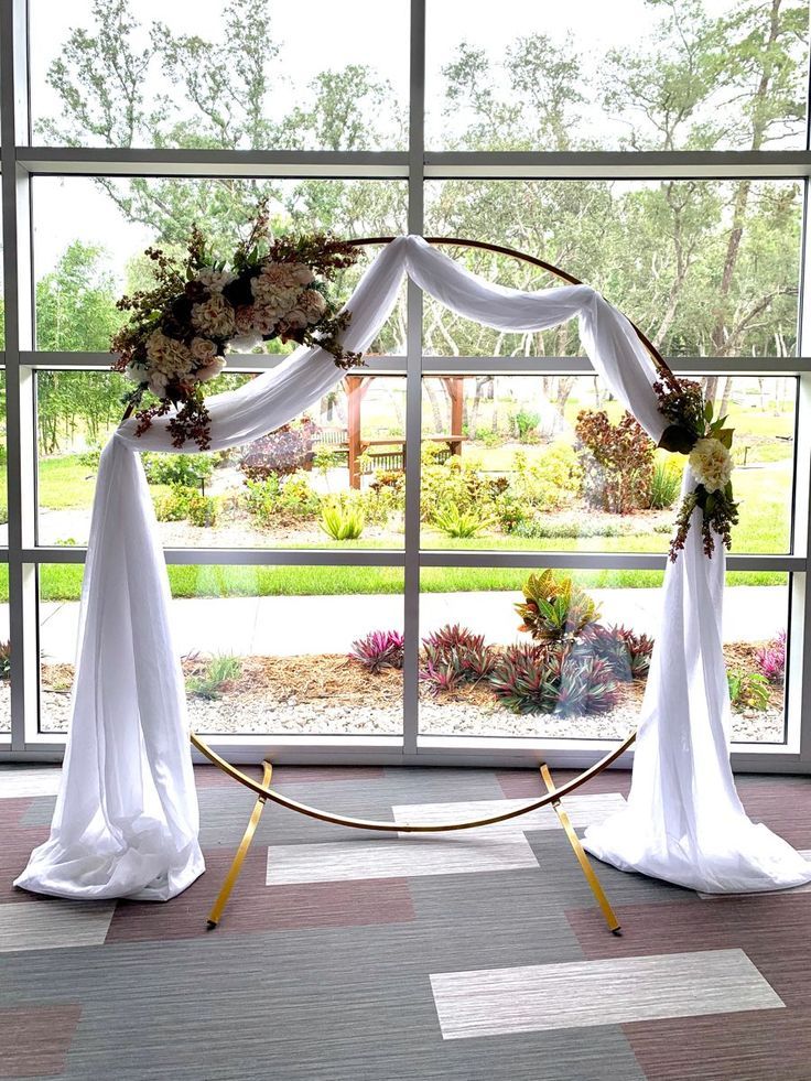 an arch decorated with flowers and greenery sits in front of a large open window