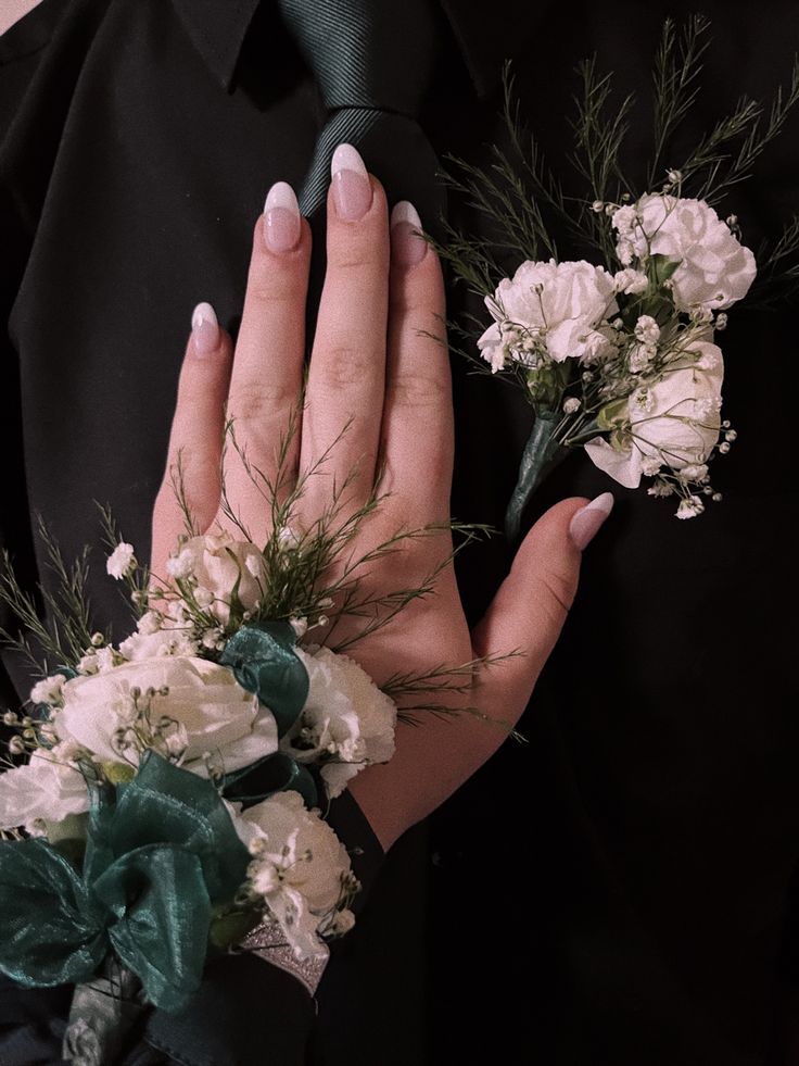 a woman holding flowers in her hands with white and green ribbons around her wrist, while wearing a black shirt