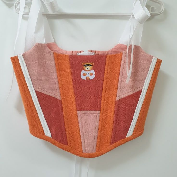 an orange and pink baby carrier hanging on a white hanger next to a wall