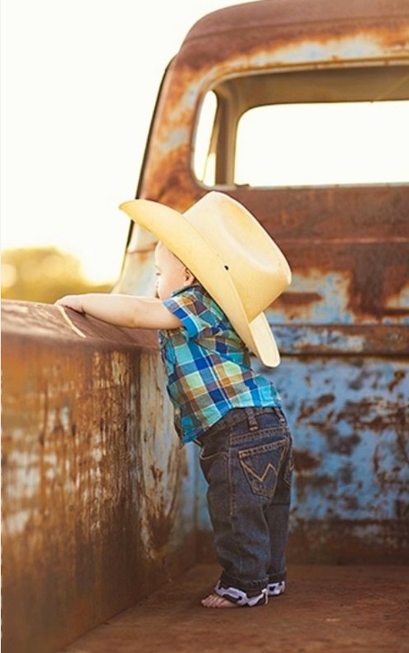 a little boy wearing a cowboy hat standing in the back of an old truck