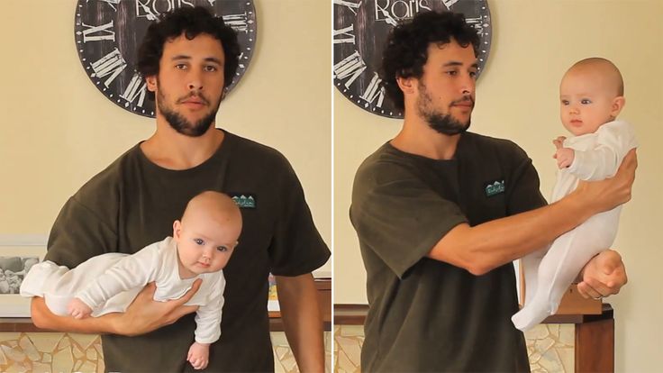 a man holding a baby in front of a wall with a clock on it's face