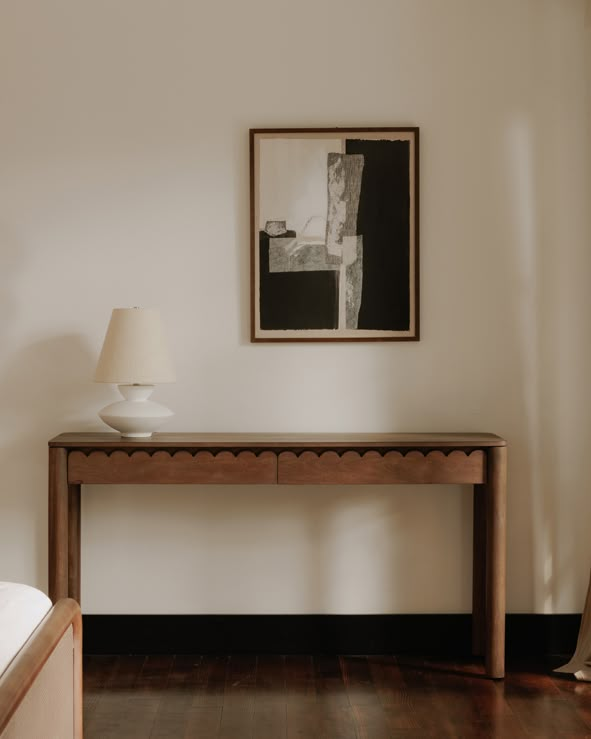 a wooden table with a lamp on top of it next to a painting and a bed