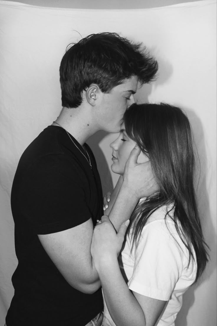 two people standing next to each other in front of a white wall and one is kissing the other