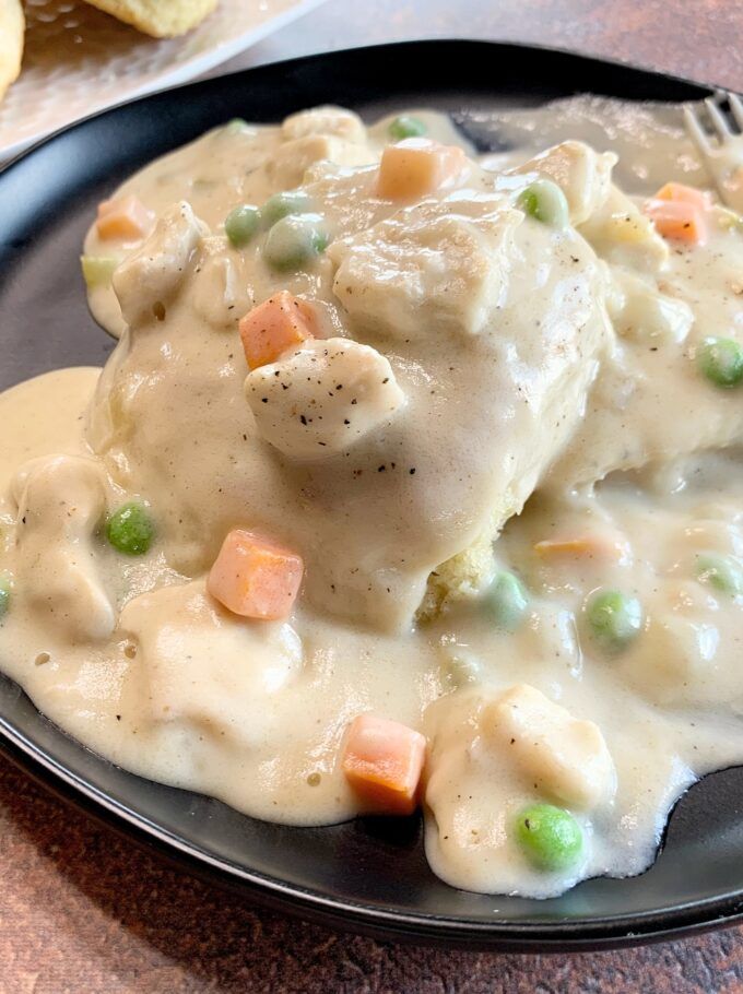 a black plate topped with chicken and gravy on top of a wooden table