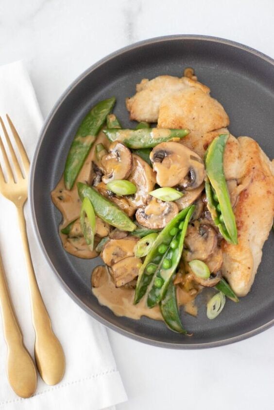 a black plate topped with chicken, mushrooms and asparagus next to a fork