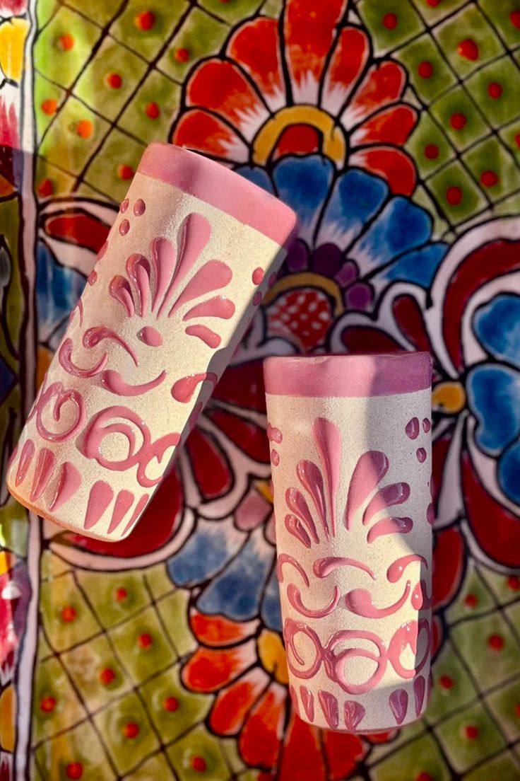 two pink and white cups sitting next to each other on a colorful wallpapered surface