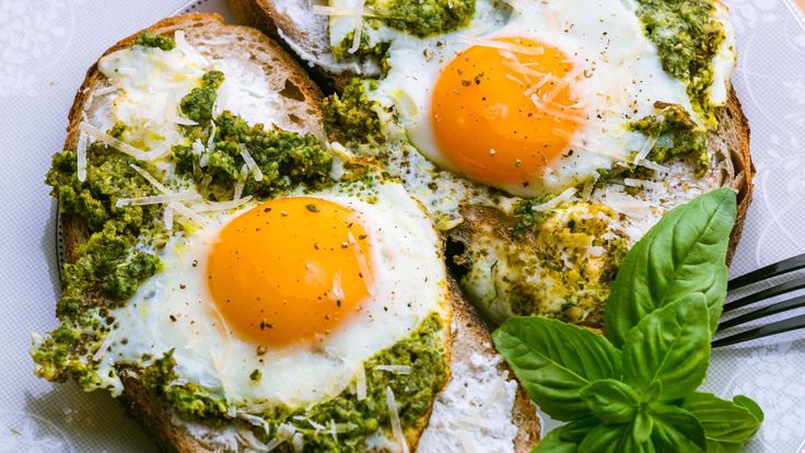 two eggs are on top of bread with pesto and parmesan cheese in the middle