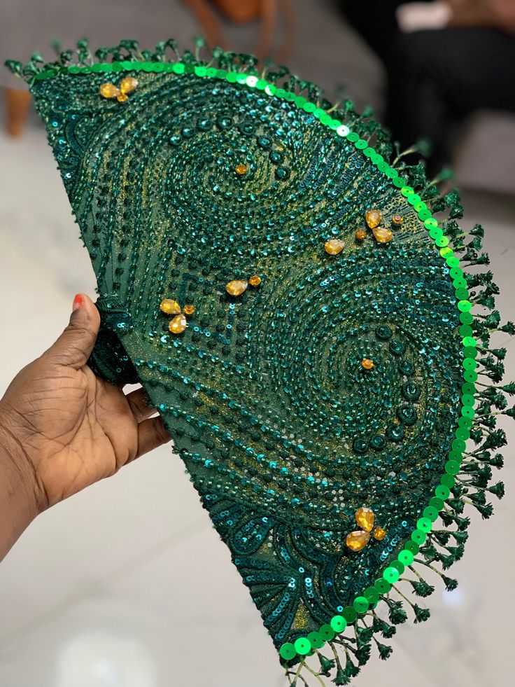 a hand holding an umbrella with green beads and beadings on it's side