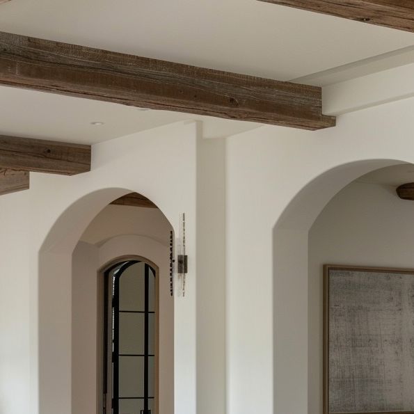 an arched doorway in a white room with wood beams on the ceiling and wooden flooring