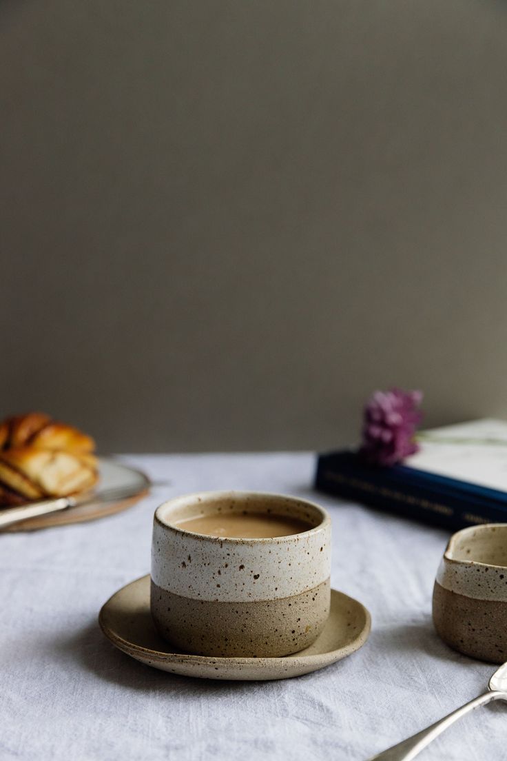 there is a cup and saucer on the table next to two plates with pastries