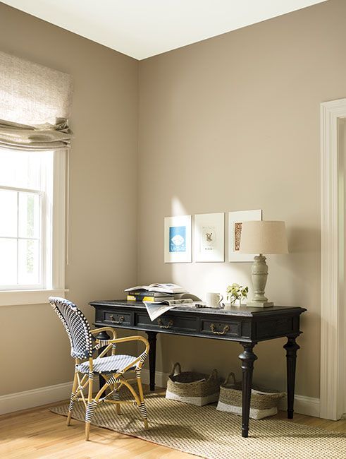 a room with a desk, chair and lamp on it in front of a window