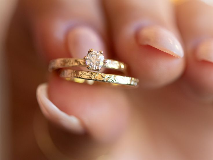 a woman's hand holding two gold wedding bands and a diamond ring on her finger